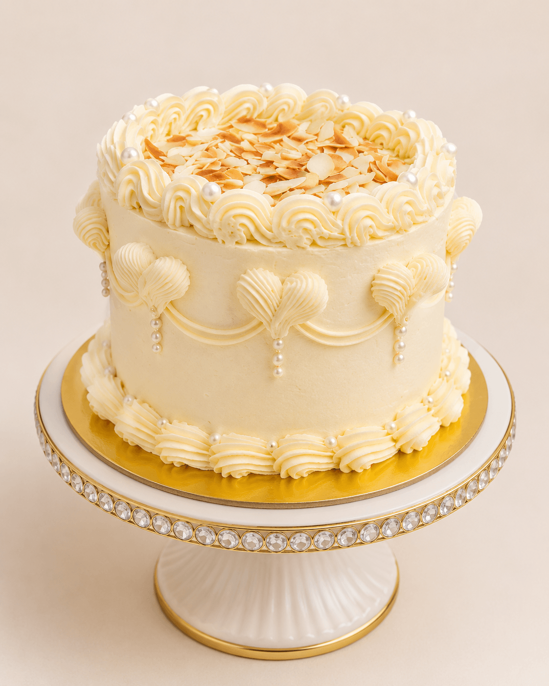 An elegant cream cake with toasted almond flakes, pearl detailing and gold accents, handcrafted by Glory Treats